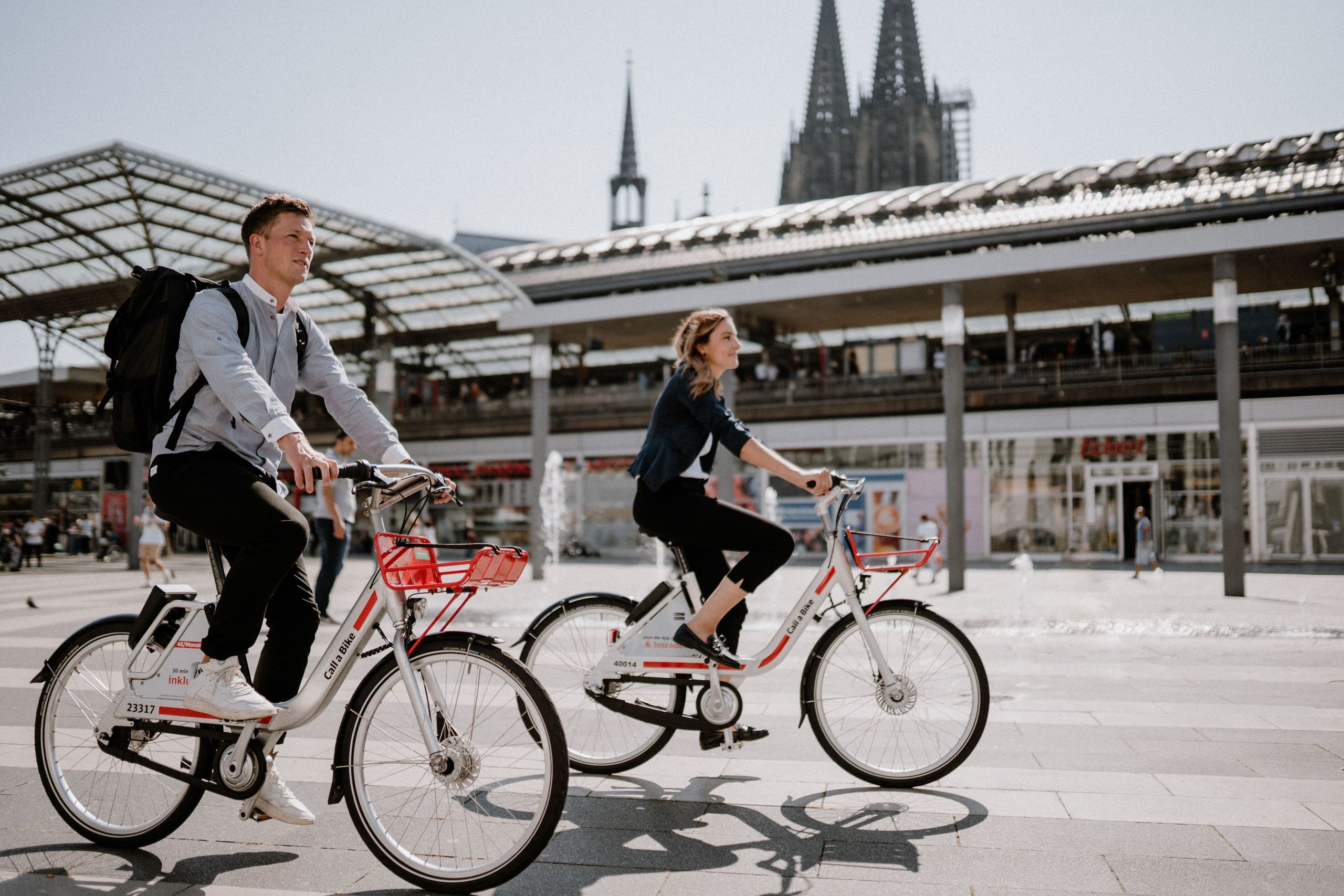 Man and woman ride their Call a Bike bikes from the station