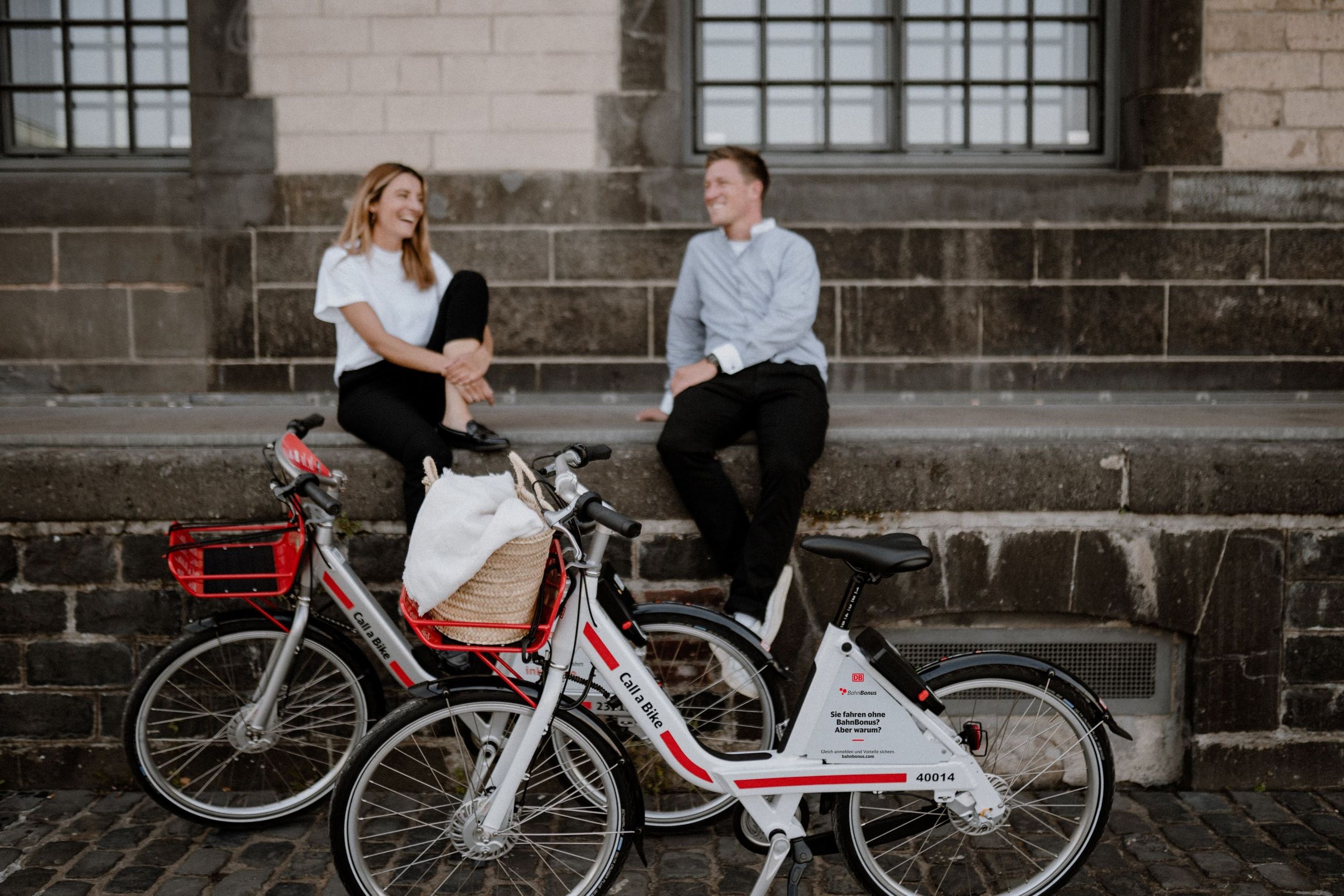 A woman and a man sit on a wall, two Call a Bikes stand in front of them